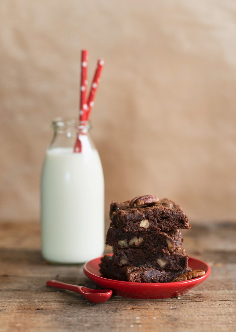 A stack of chocolate and nut brownies in front of a milk bottle