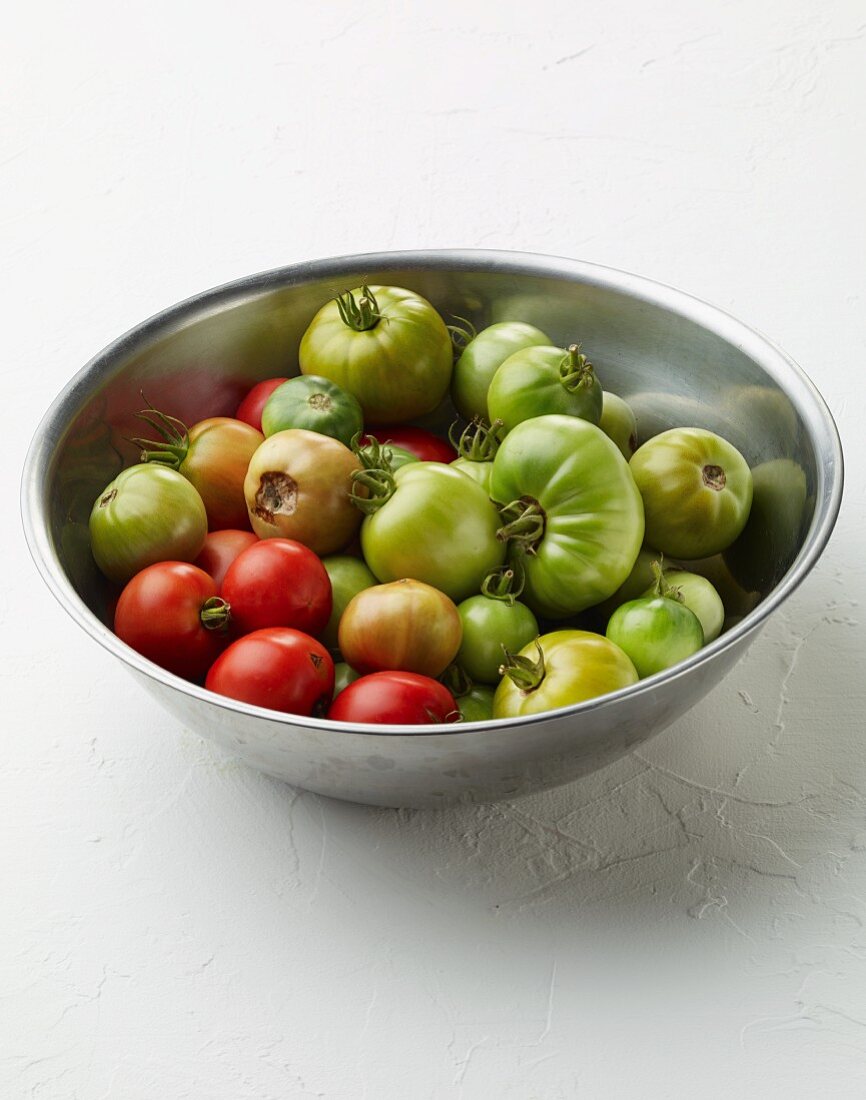 Green and red tomatoes in a stainless steel bowl