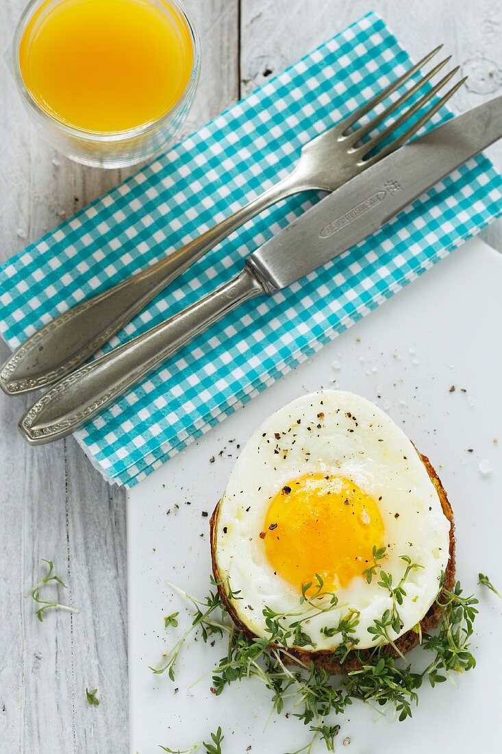 A fried egg on toast with cress and orange juice