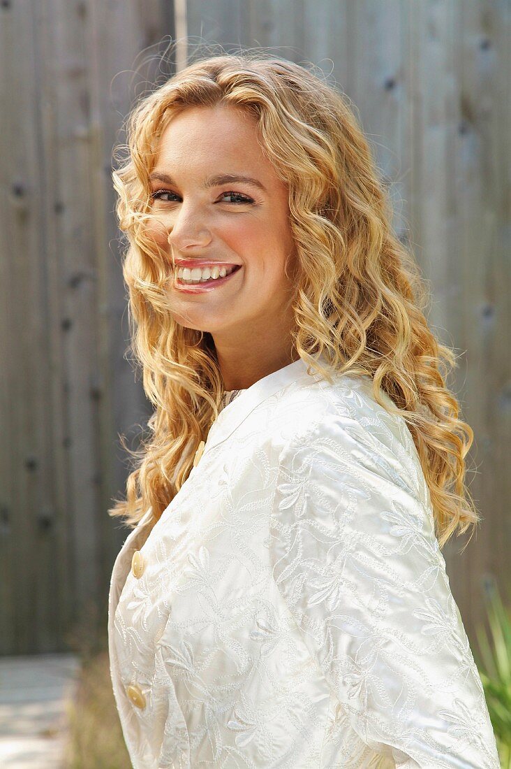 A young blonde woman outside wearing a white coat