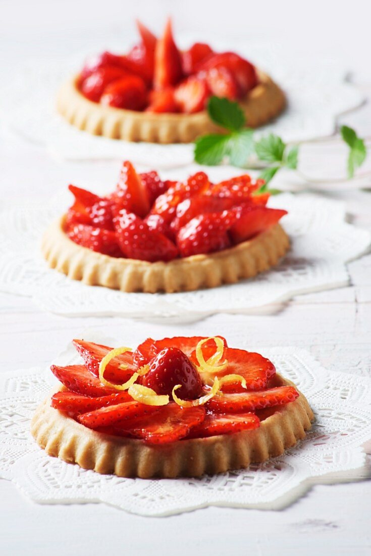 Three strawberry tartlets with lemon zest on doilies