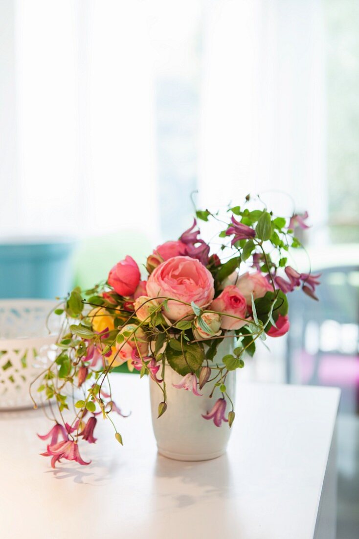 Blumenstrauss mit englischen Duftrosen und Clematis und anderen Blumensorten in weisser Vase auf Tisch