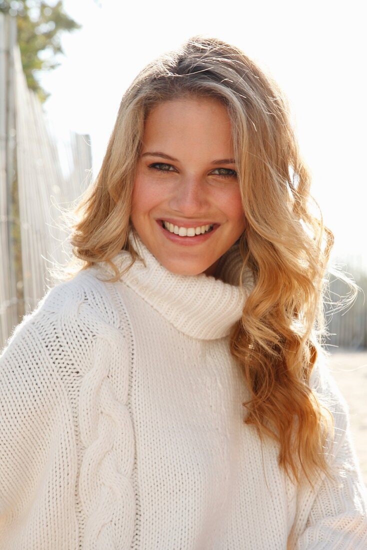 A young blonde woman wearing a white knitted roll-neck jumper