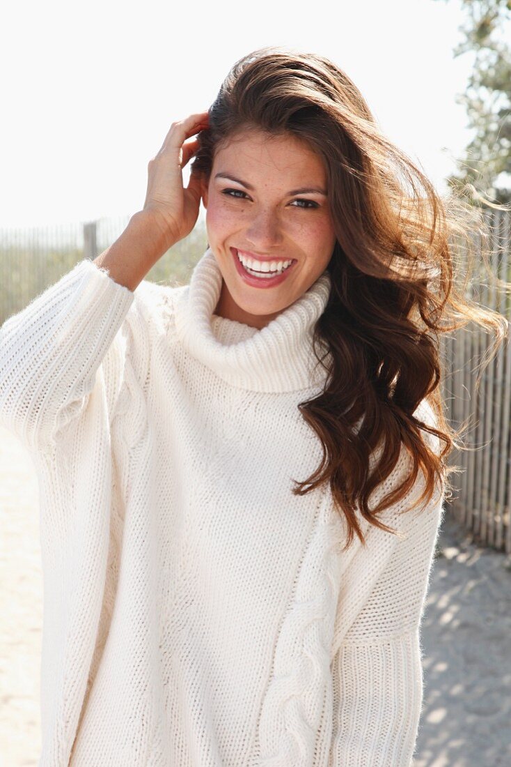 A young brunette woman outside wearing a white knitted roll-neck jumper
