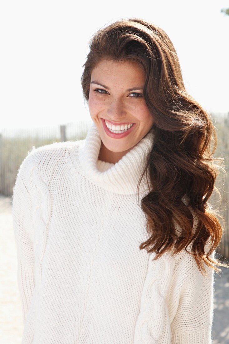 A young brunette woman outside wearing a white knitted roll-neck jumper