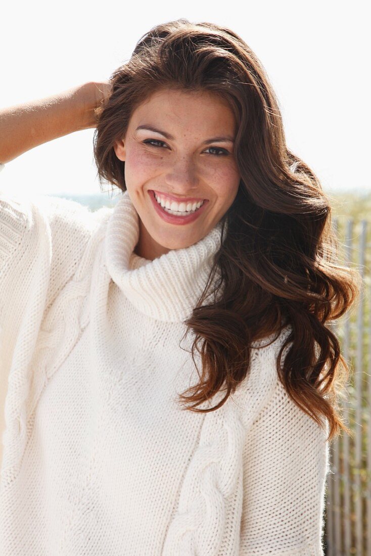 A young brunette woman outside wearing a white knitted roll-neck jumper