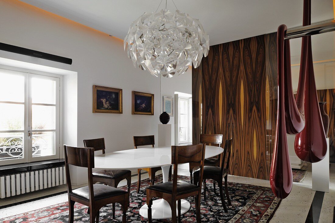 Heller Essraum mit weißem Designer-Esstisch und antiken Stühlen; an den Wänden goldgerahmte Ölgemälde und moderne Kunst