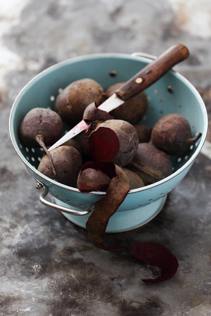 Cooked beetroots in a colander, one partially peeled