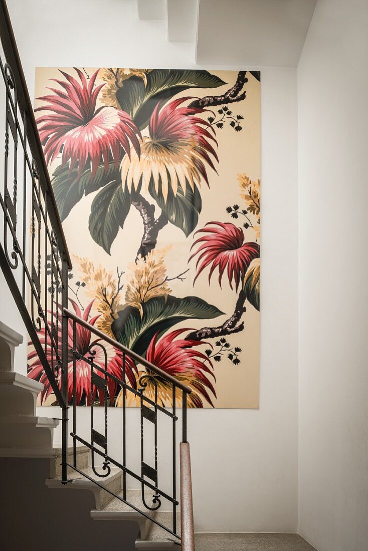 Large, floral artwork on white wall in stairwell with Art Nouveau metal balustrade
