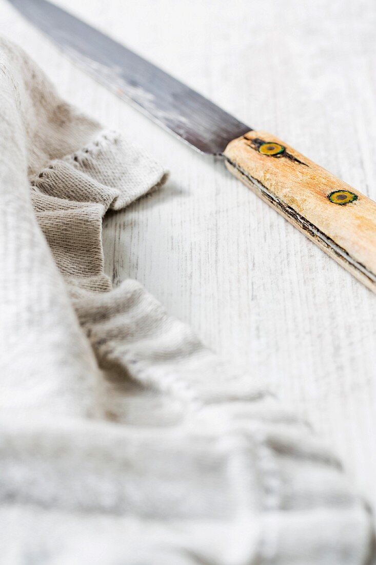 Altes Messer und rustikales Geschirrtuch auf Holzuntergrund