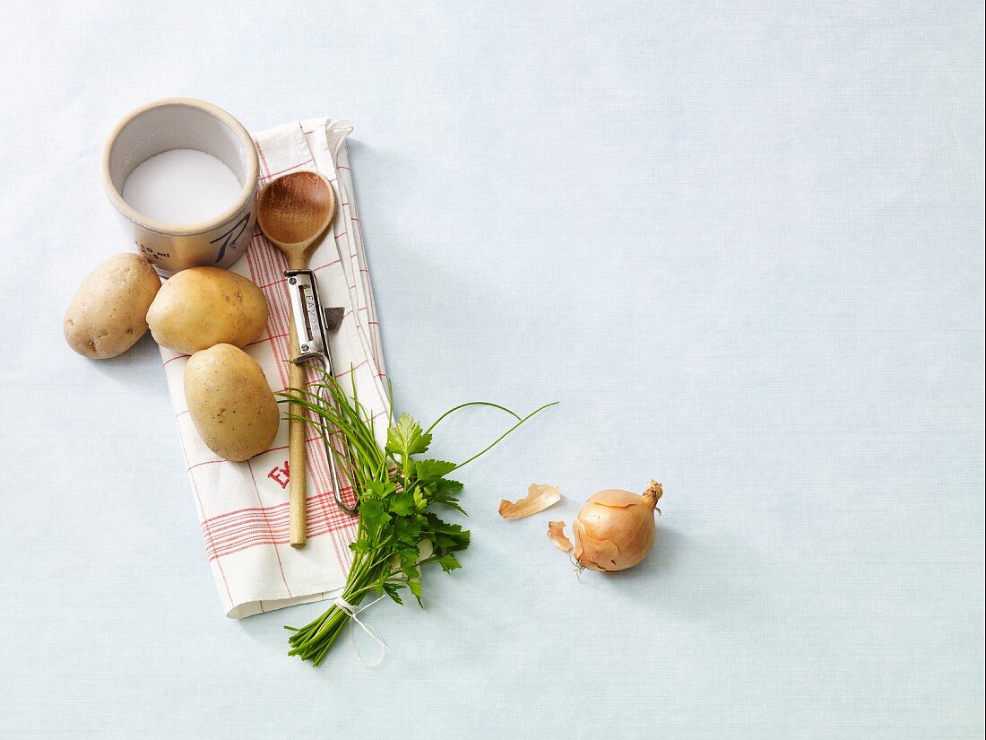 An arrangement of potatoes, herbs, onions and kitchen utensils