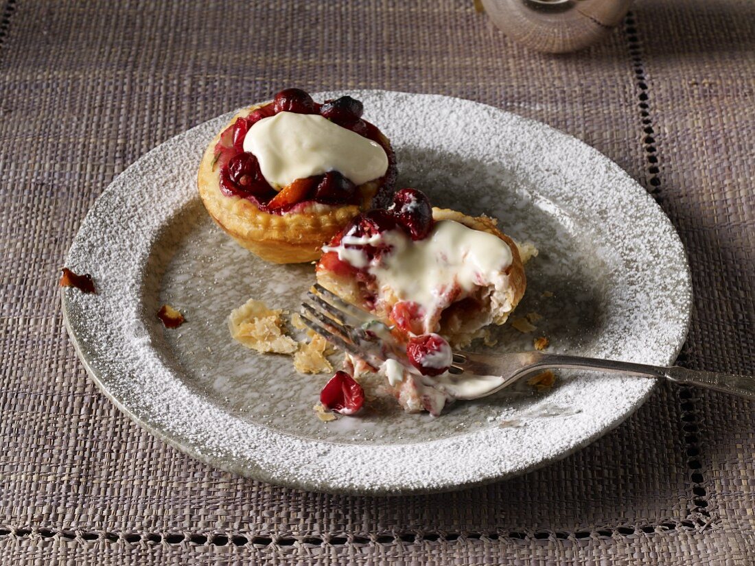 Two cranberry tartlets on a plate with cream, one half eaten