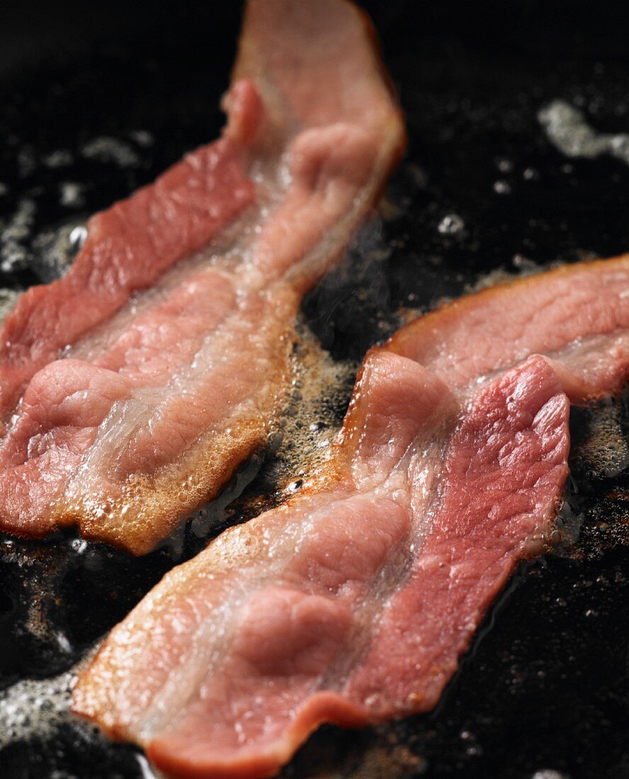 A close-up of bacon frying in a pan
