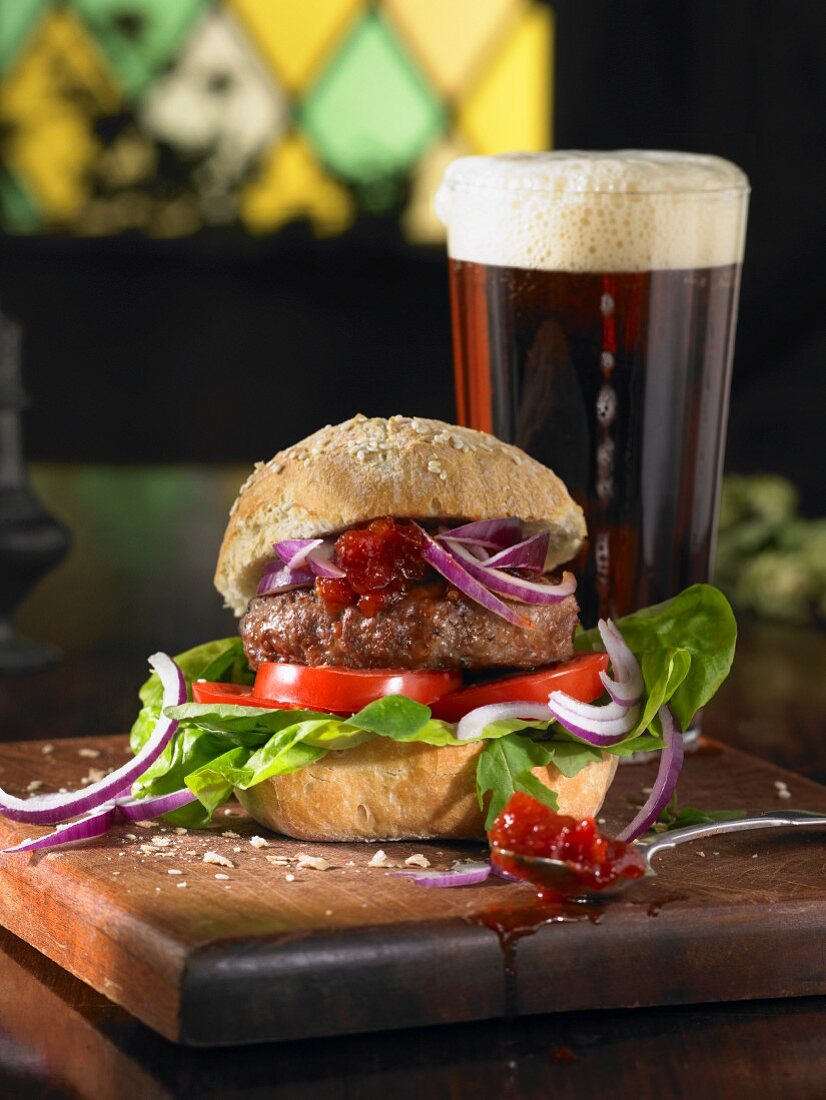 A burger with lettuce, tomatoes, red onions and chutney served with a pint of ale