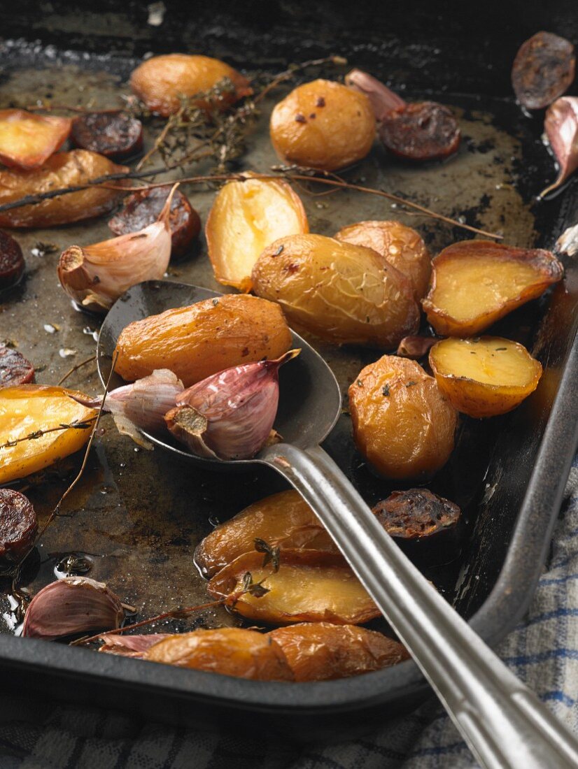 Roast new potatoes, chorizo and garlic on a baking tray