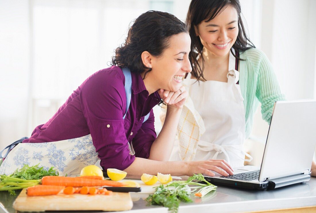 Two women using a laptop and cooking together