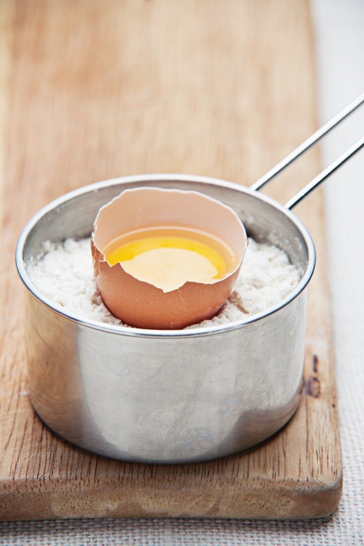 Aufgeschlagenes Ei in einem Topf mit Mehl