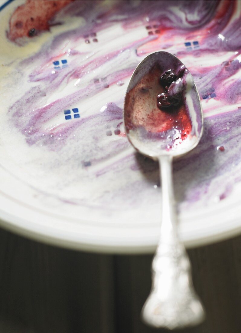 A spoon on a dessert plate with the remains of blueberry crumble and ice cream