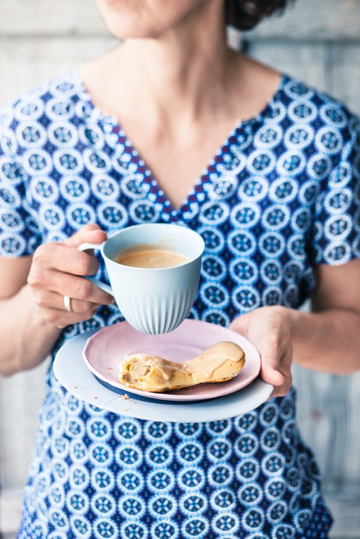 A woman with a cup of coffee and an eclair filled with coffee cream