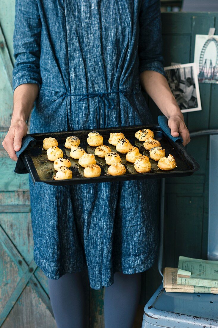 Frau hält Backblech mit Gougeres (Käsewindbeutel, Frankreich)