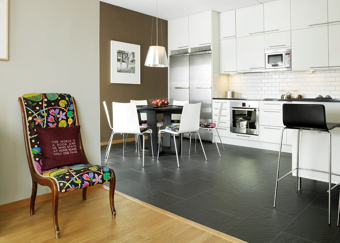 Retro chair with colourful upholstery in front of white kitchen-dining room with black accents and charcoal floor tiles