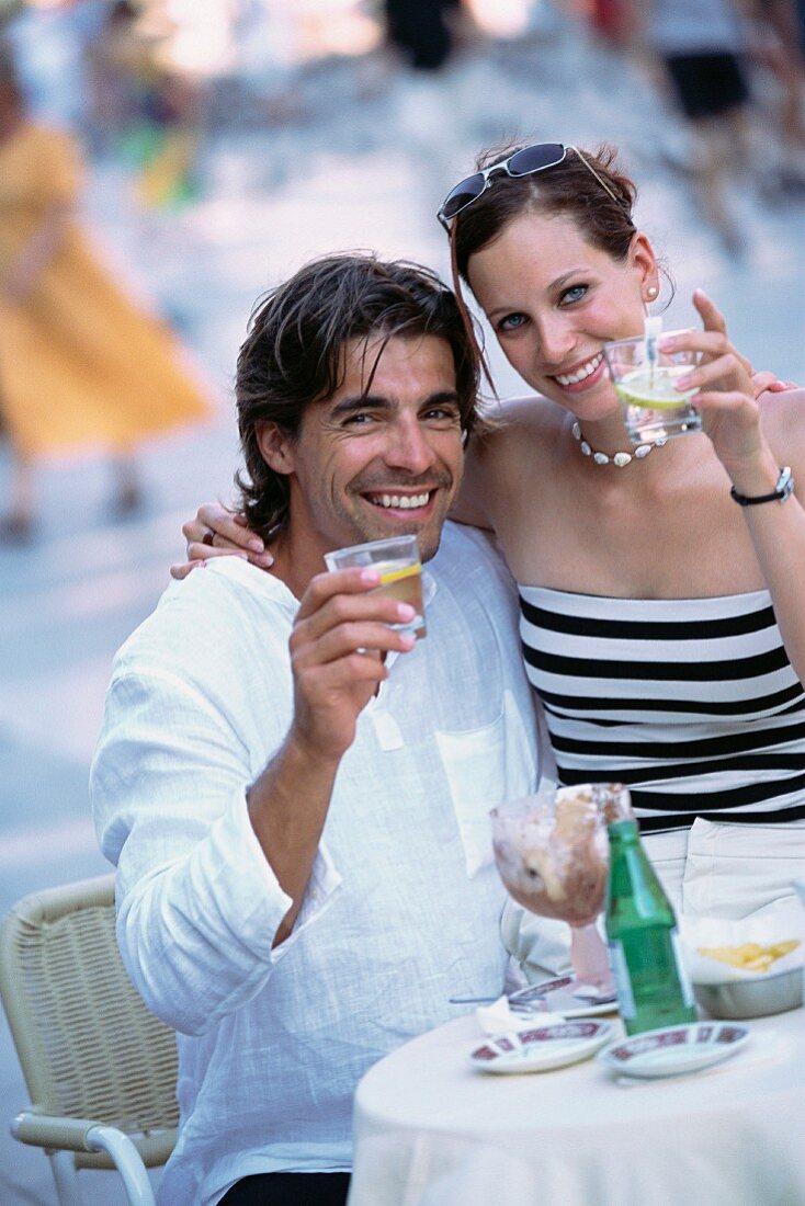 A couple at a pavement cafe raising their glasses