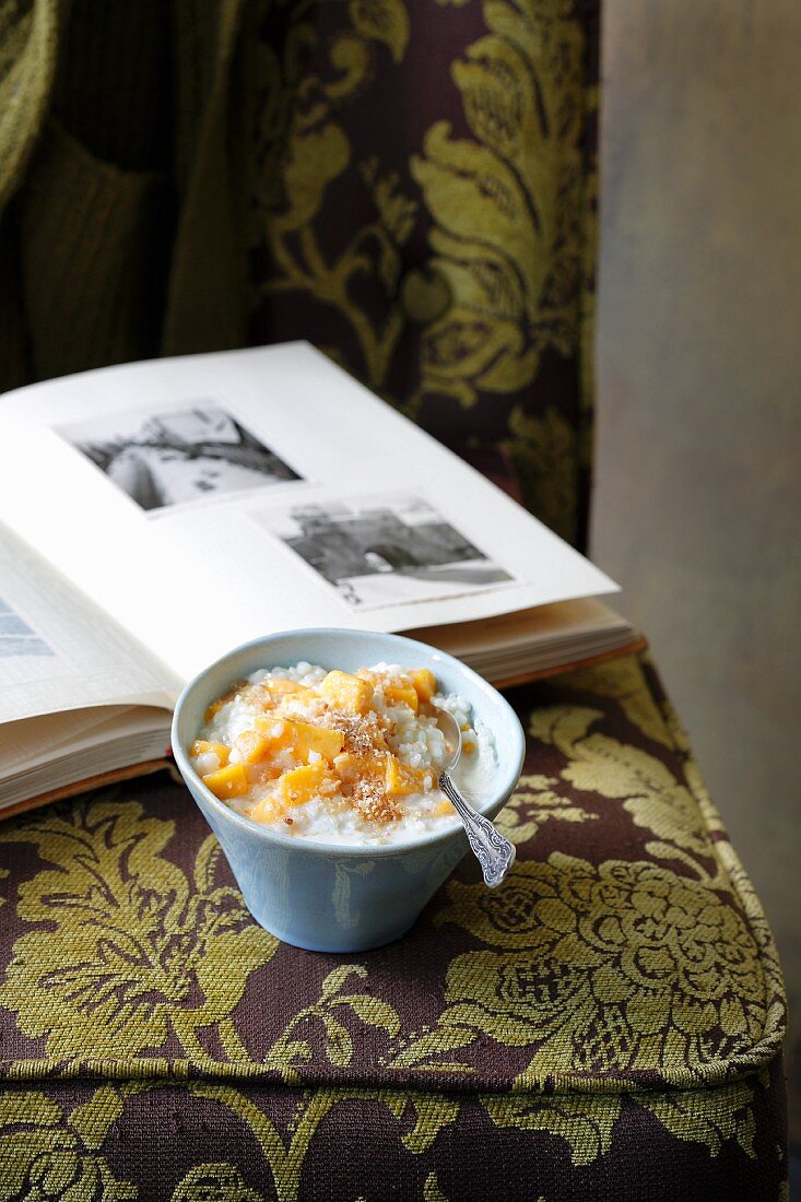 Kokos-Milchreis mit Mango auf Polstersessel vor Fotoalbum