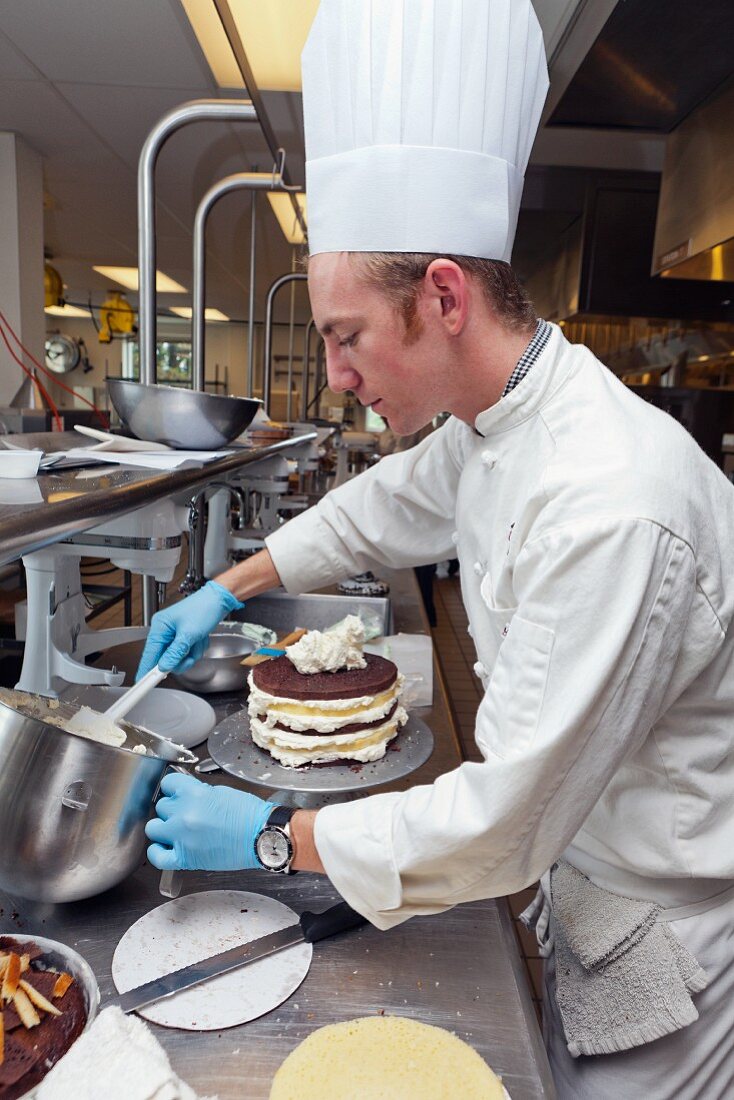 A chef decorating a layer cake with frosting