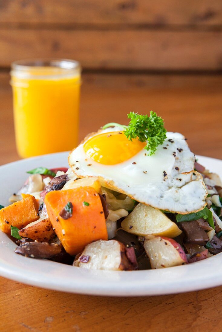 A fried egg on a bed of fried potatoes mushrooms turnips served with orange juice (USA)