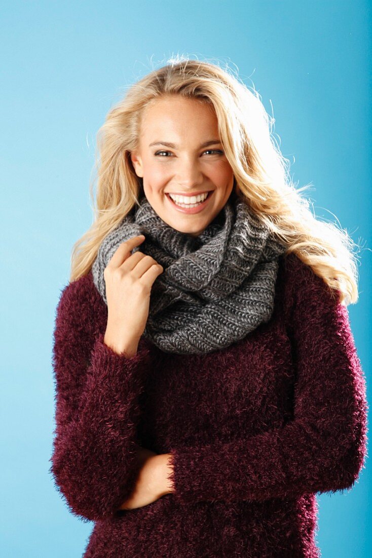 A young blonde woman wearing a burgundy knitted jumper and a grey scarf