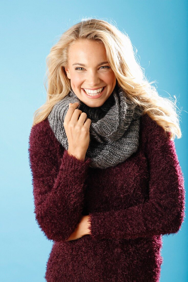 A young blonde woman wearing a burgundy knitted jumper and a grey scarf