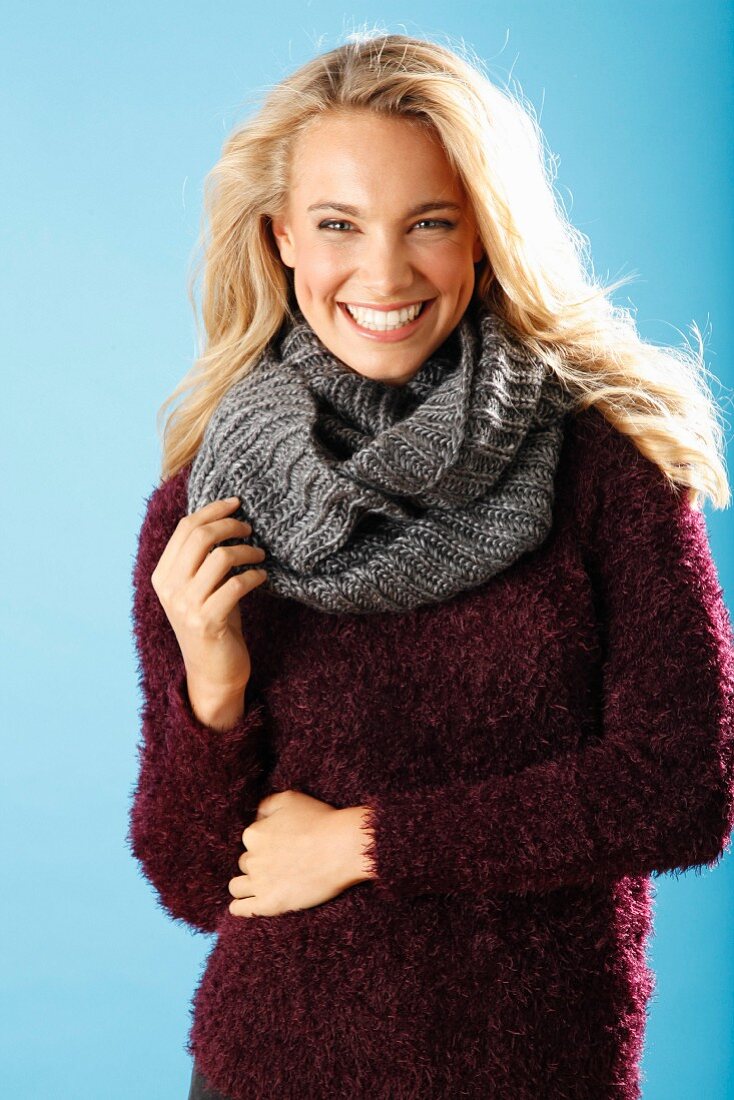 A young blonde woman wearing a burgundy knitted jumper and a grey scarf