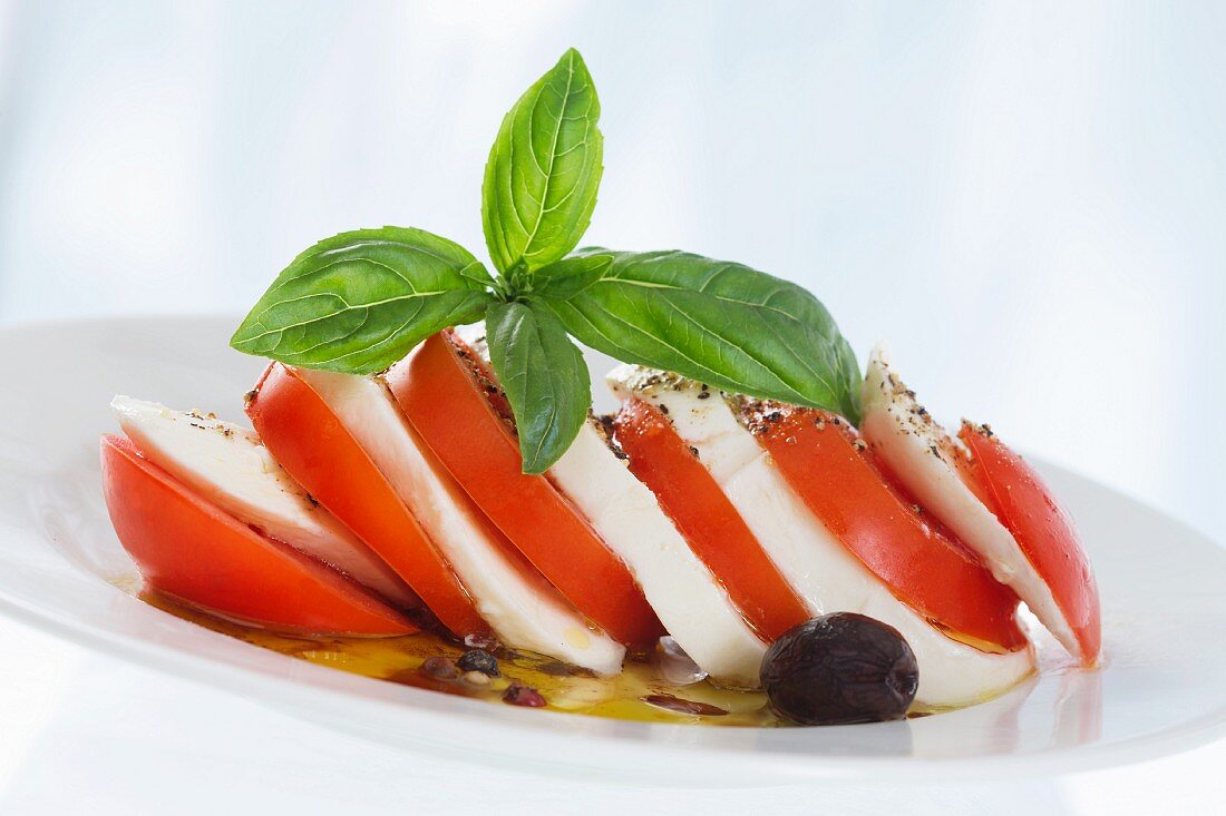 Geschichtete Tomaten mit Mozzarella, Basilikum und Oliven