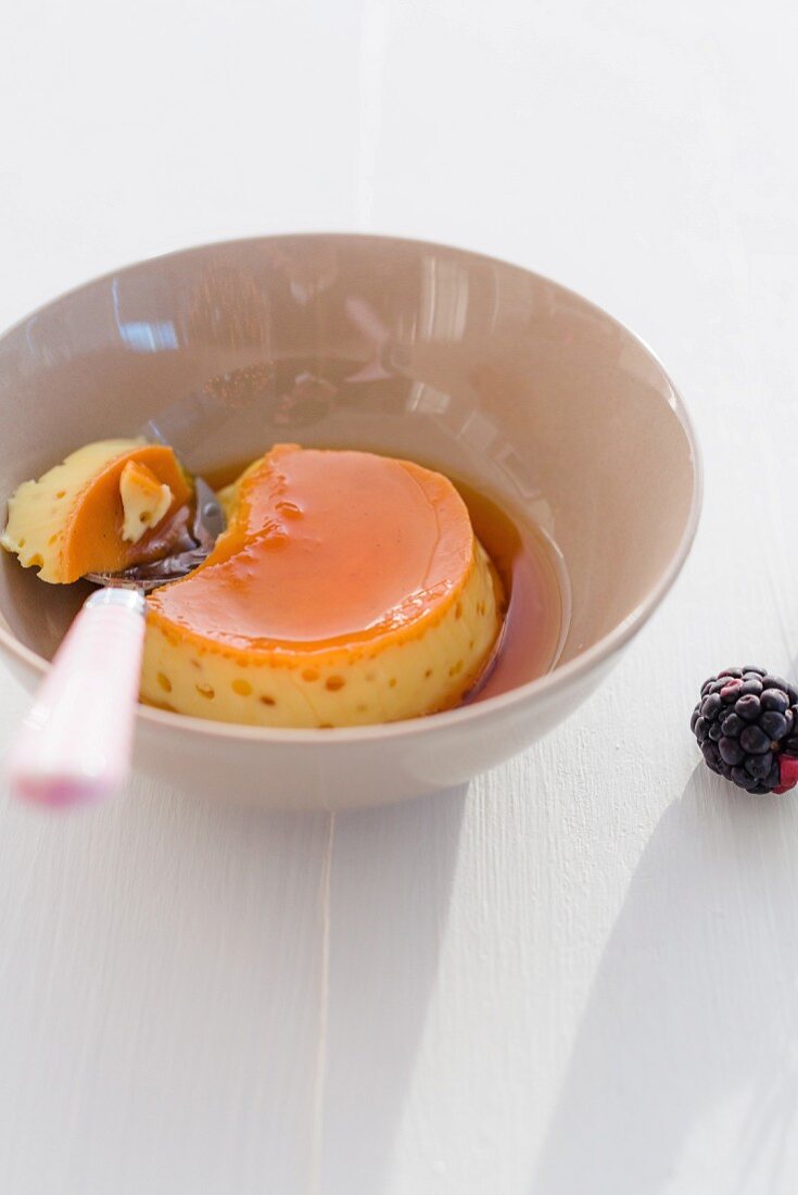 A bowl of creme caramel with a bite taken out