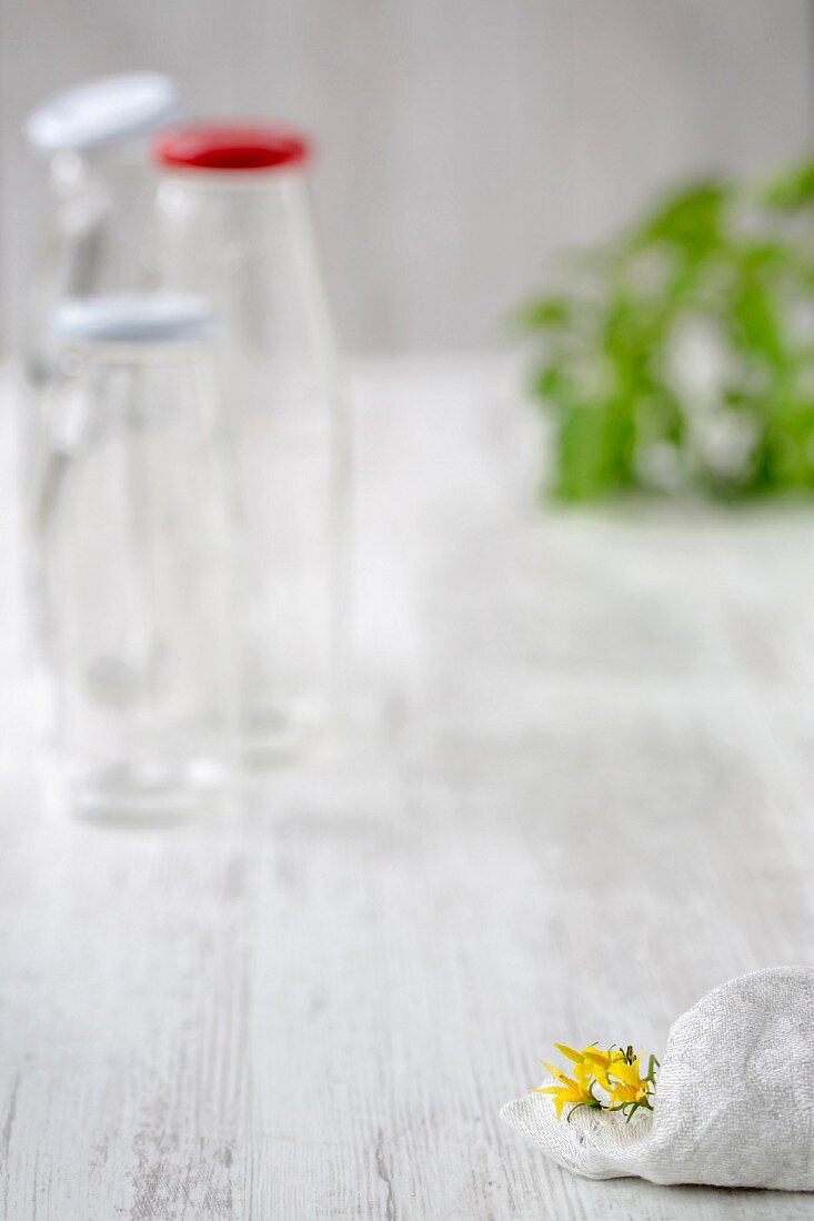 Empty glass bottles, tomato leaves and a kitchen cloth on a wooden surface
