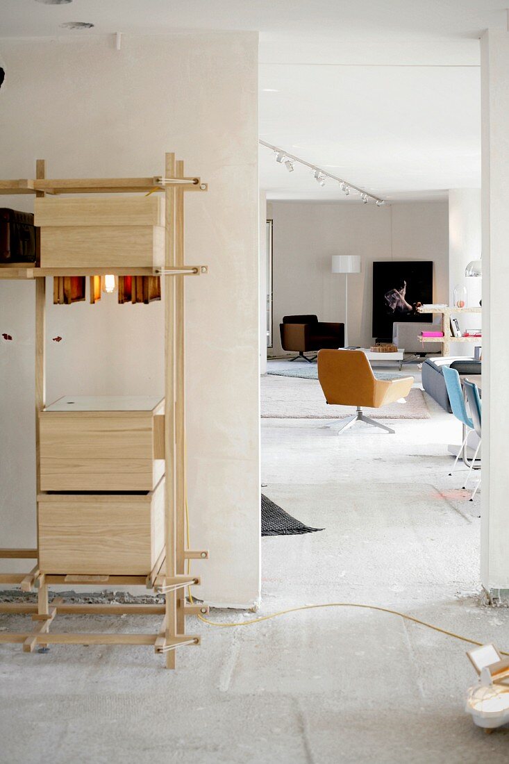 Boxes on simple, wooden DIY shelves next to open doorway with view of swivel chair in loft-style interior