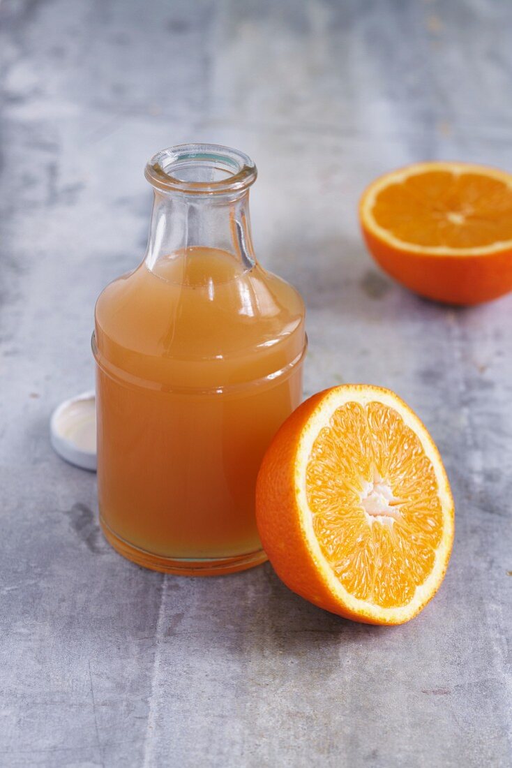 A bottle of apple juice and a halved orange