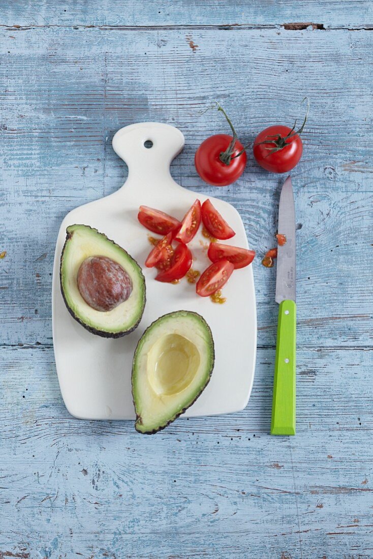 A halved avocado and tomatoes on a chopping board