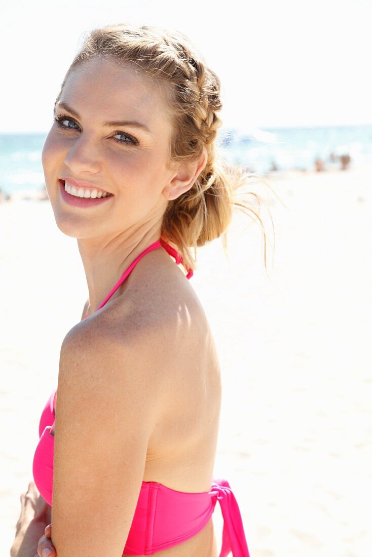 A young blonde woman on a beach wearing a pink bikini top