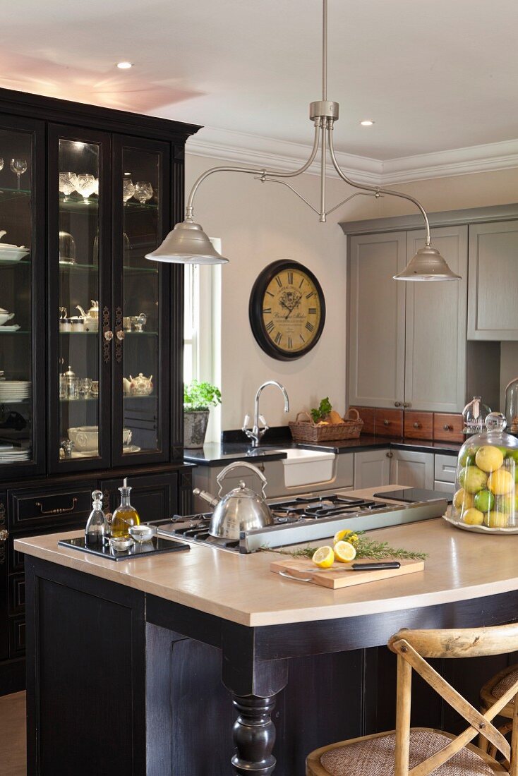 Detail of kitchen island below vintage pendant lamp; antique display cabinet with spotlights in background