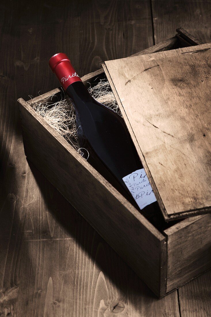 A bottle of red wine in an open wooden crate