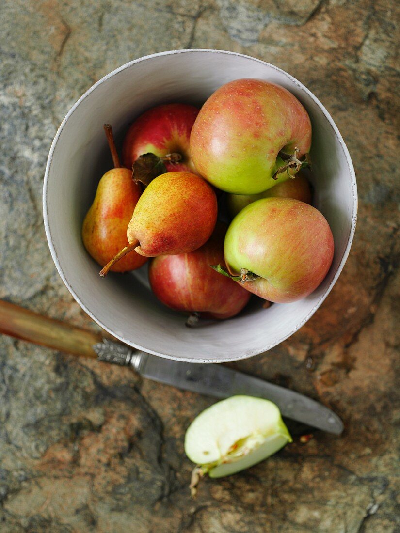 A bowl of apples and pears with a knife and an apple wedge next to it