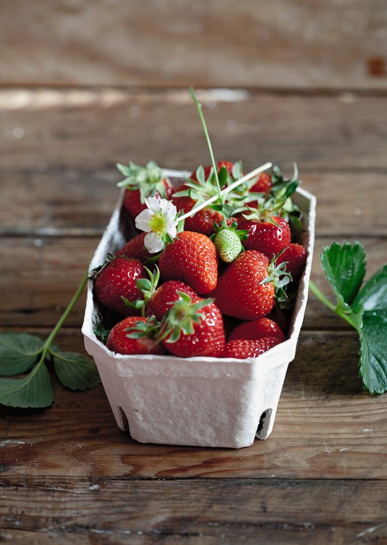 Strawberries with leaves and flowers in a cardboard punnet