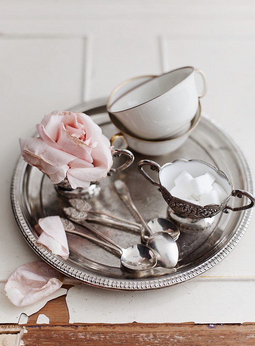 Teetassen, Zuckerdose, Löffel und Rosenblüte auf Silbertablett