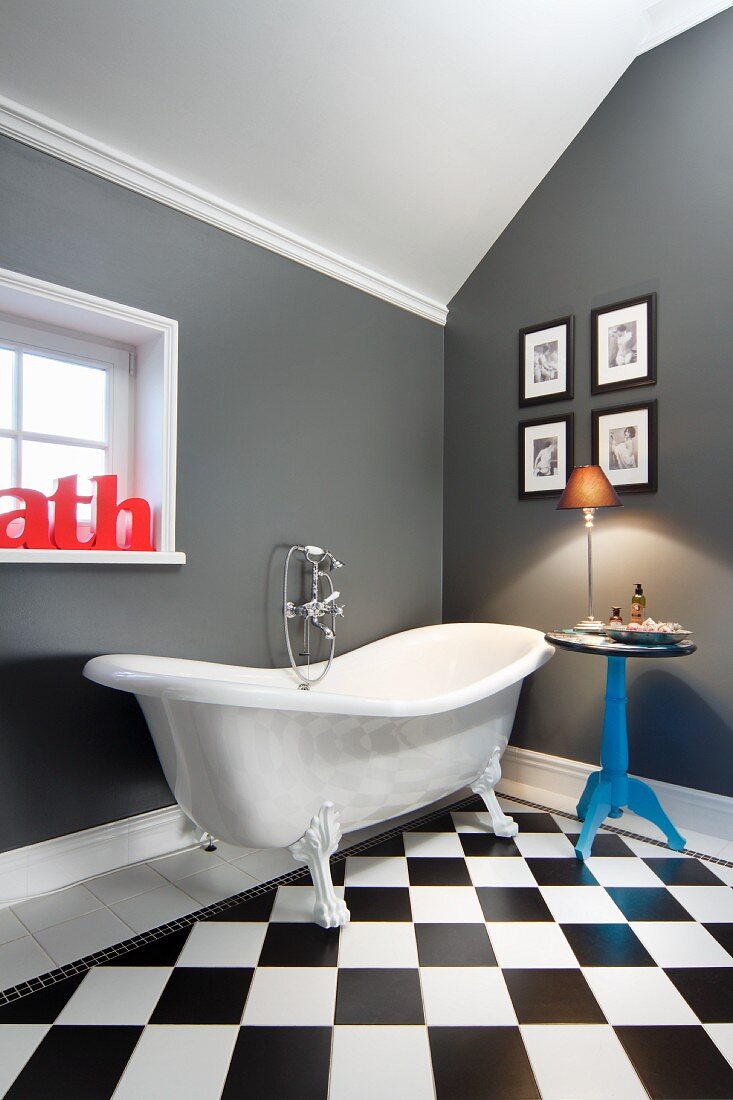 Elegant bathroom with side table and gallery of pictures next to claw-foot bathtub