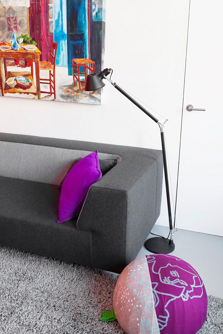 Moderne Couch mit grauem Filzbezug, violettes Kissen, Sitzpouf vor schwarzer Tolomeo Stehleuchte