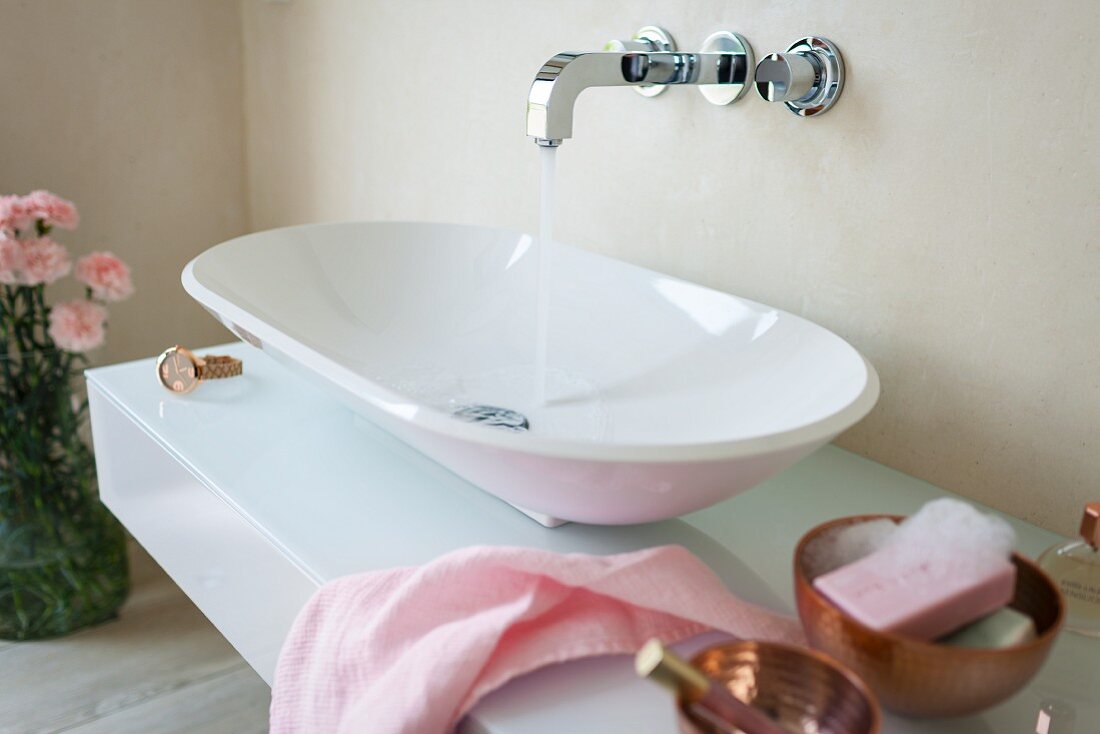 A designer console basin on a washstand with a glass surface and a wall tap