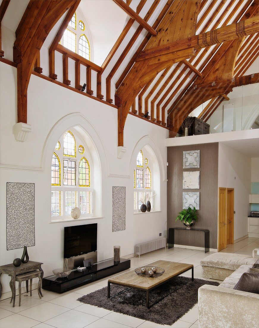 Contemporary interior with lounge furnishings in former church nave with Gothic-style windows and exposed roof structure