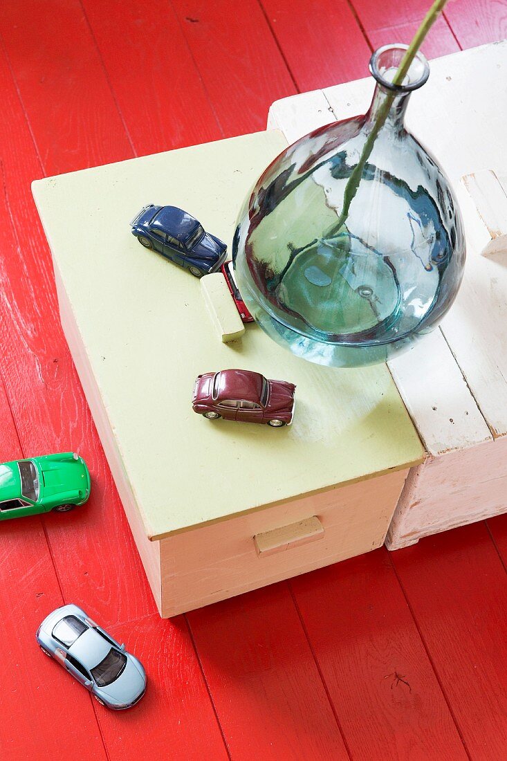 Glass vase and toy cars on wooden trunk and on red-painted wooden floor