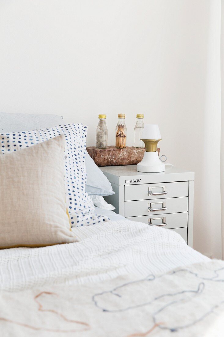 Scatter cushions on bed next to table lamp on bedside cabinet